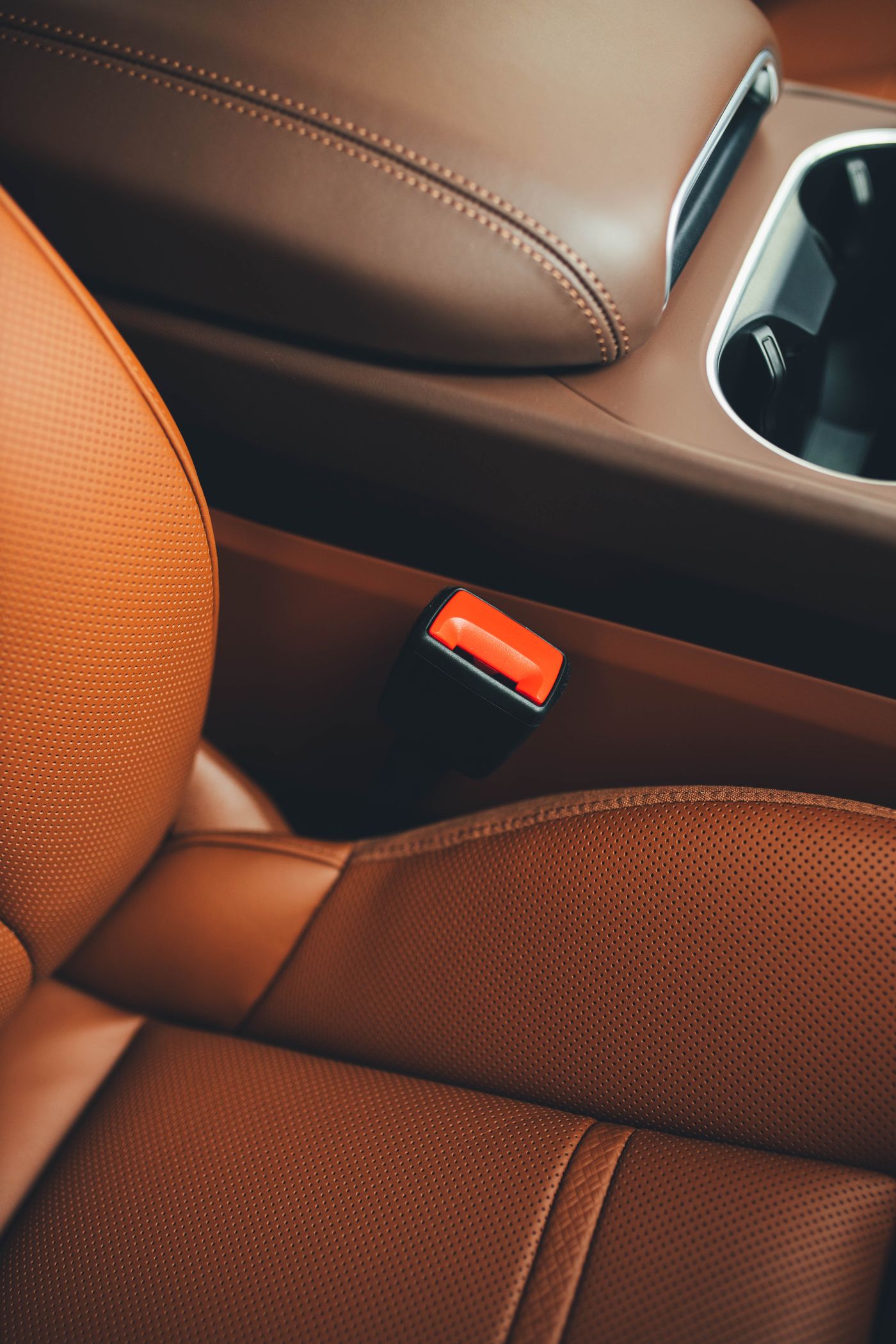 Tan perforated-leather seat and armrest with a black and orange seat-belt buckle and a cup-holder.